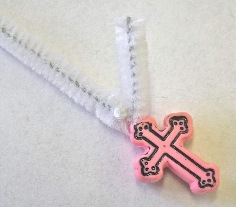 pink plastic cross bead attached to white pipe cleaner to make rosary for kids