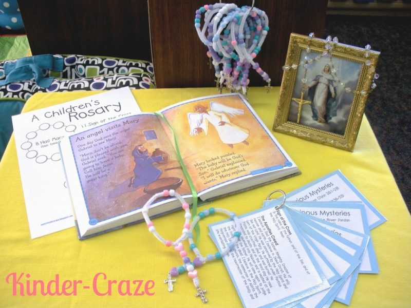 catholic classroom rosary prayer space includes a framed picture of jesus, children's rosaries, rosary prayer cards, and a book illustrating the mysteries