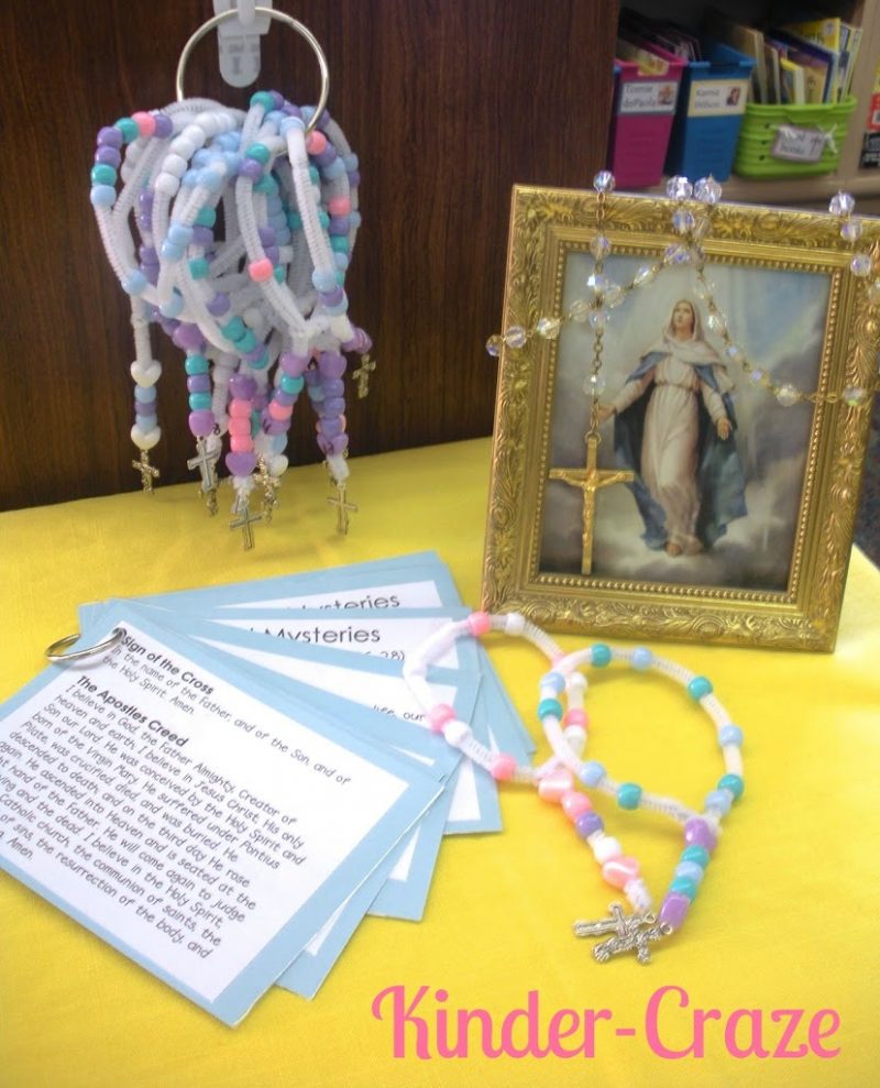 a rosary prayer space set up in a kindergarten classroom on a bright yellow table with children's rosaries, prayer cards, and framed pictures of jesus