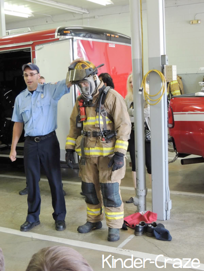 one firefighter wearing safety gear while another explains the importance of each piece