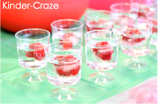 plastic stemmed cups filled with water and raspberry ice cubes sitting on top of green table cloth