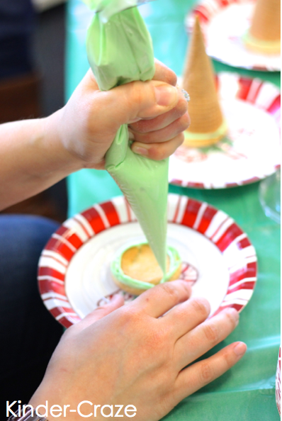 kindergarten student using piping bag to add green frosting to top of small round sugar cookie on a holiday paper plate