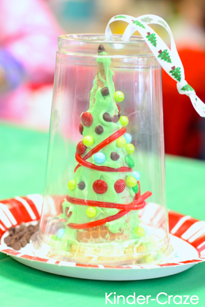 the completed kindergarten Christmas craft is a festively decorated tree sitting inside of plastic cup carrying case