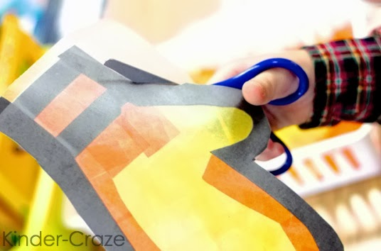 student cutting out completed orange and yellow mitten from excess contact paper