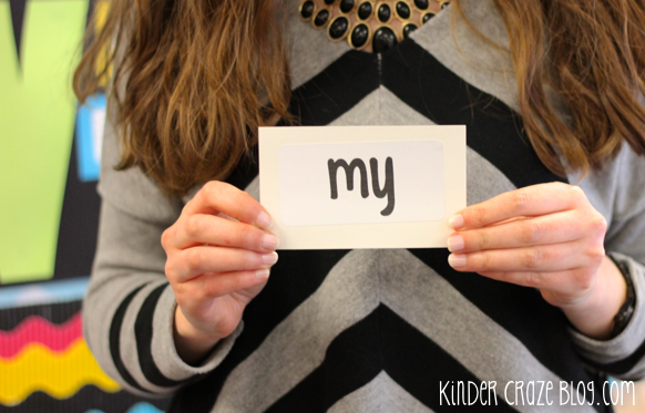 teacher holding black and white flashcard of sight word "my" in the classroom