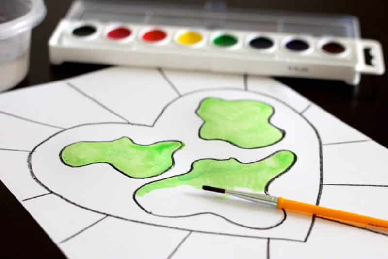 using green watercolors to paint the land on heart-shaped earth drawing