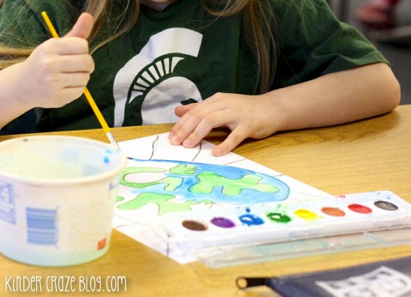 child painting earth shaped like a heart with blue and green watercolor paints