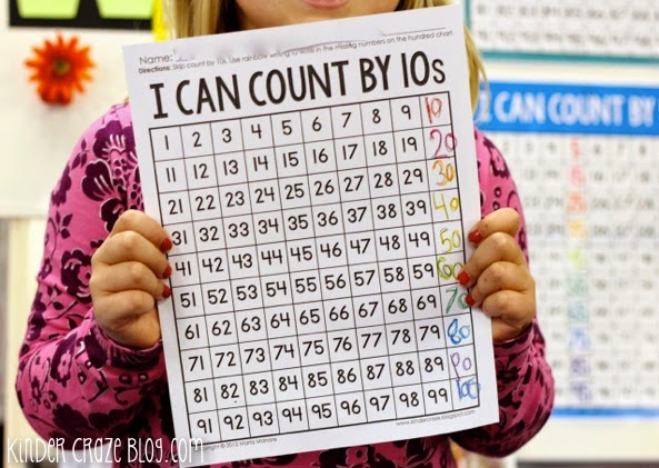 kindergarten student holding "I can count by 10s" worksheet completed with rainbow colored markers