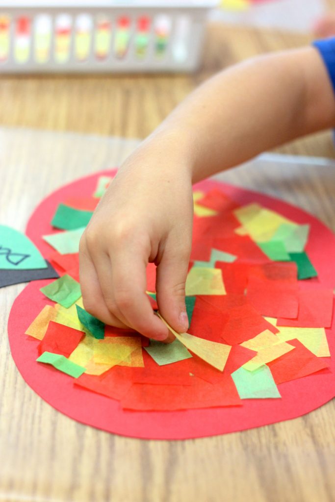 child making apple craft with red, green, and yellow tissue paper squares