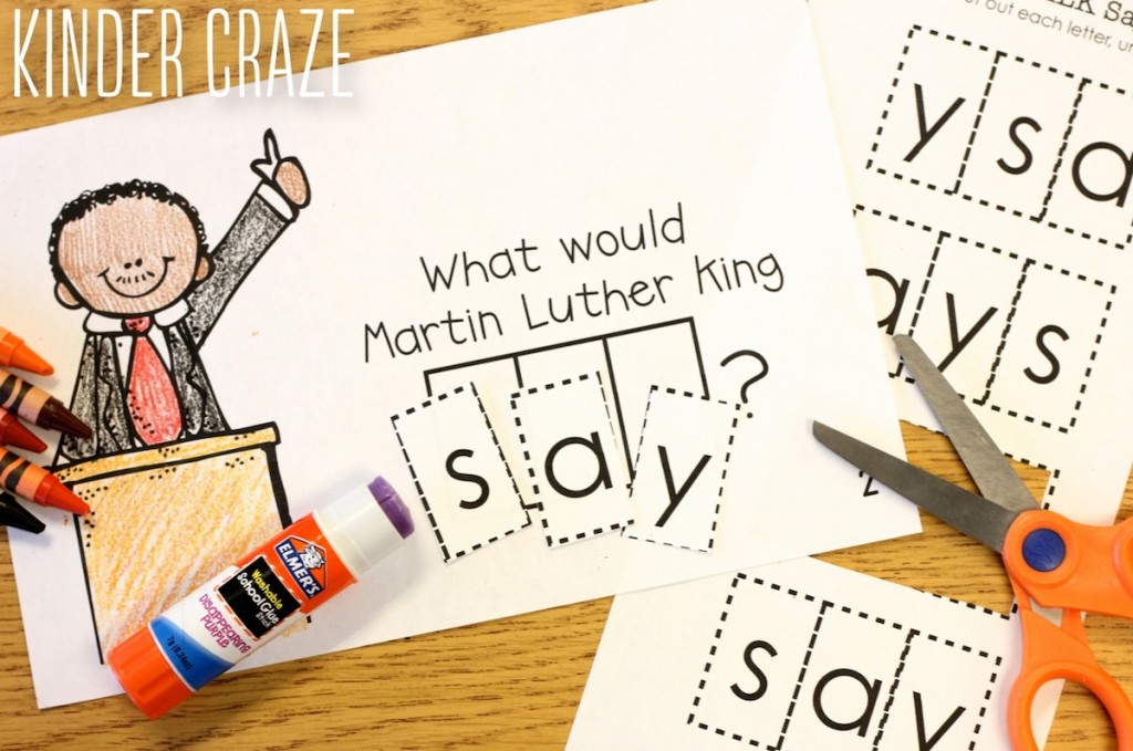 a page from the MLK interactive reader sitting on student desk with a nicely colored picture and the letters of the word "say" glued down in order to complete the sentence "What would Martin Luther King say?" a glue stick and scissors are placed on top of work