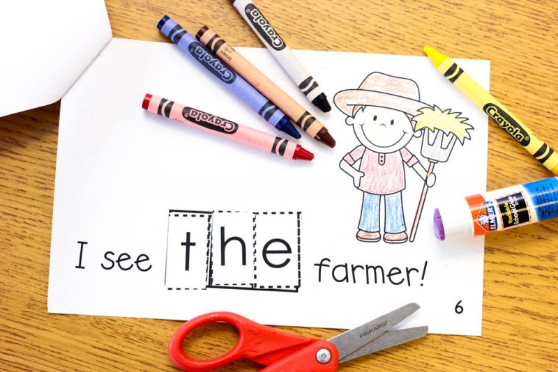 cut and paste reader on student's desk surrounded by crayons, scissors, and a glue stick letters of the word the are glued down to build the sentence "I see the farmer"