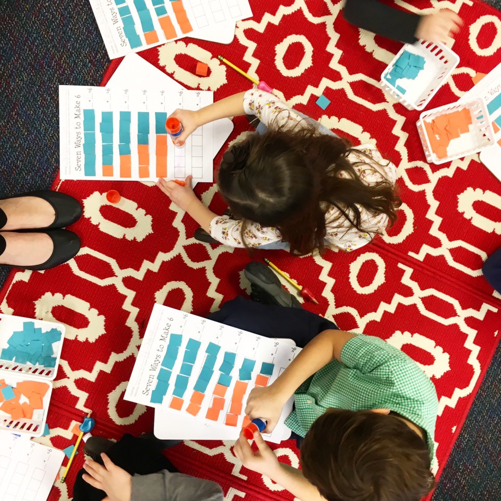 students sitting on red carpet in kindergarten classroom using paper squares to show patterns in decomposing numbers
