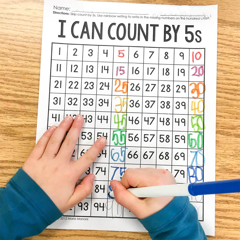 kindergarten student using markers to write rainbow numbers on skip counting by 5s worksheet