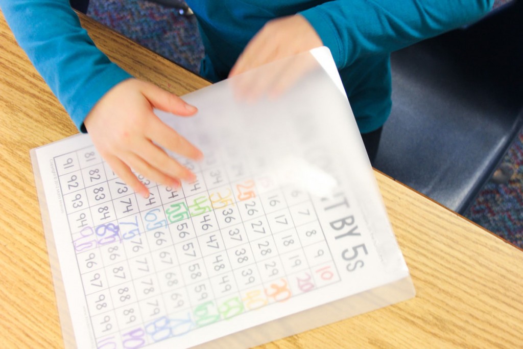 child placing completed skip counting chart in a laminating sheet