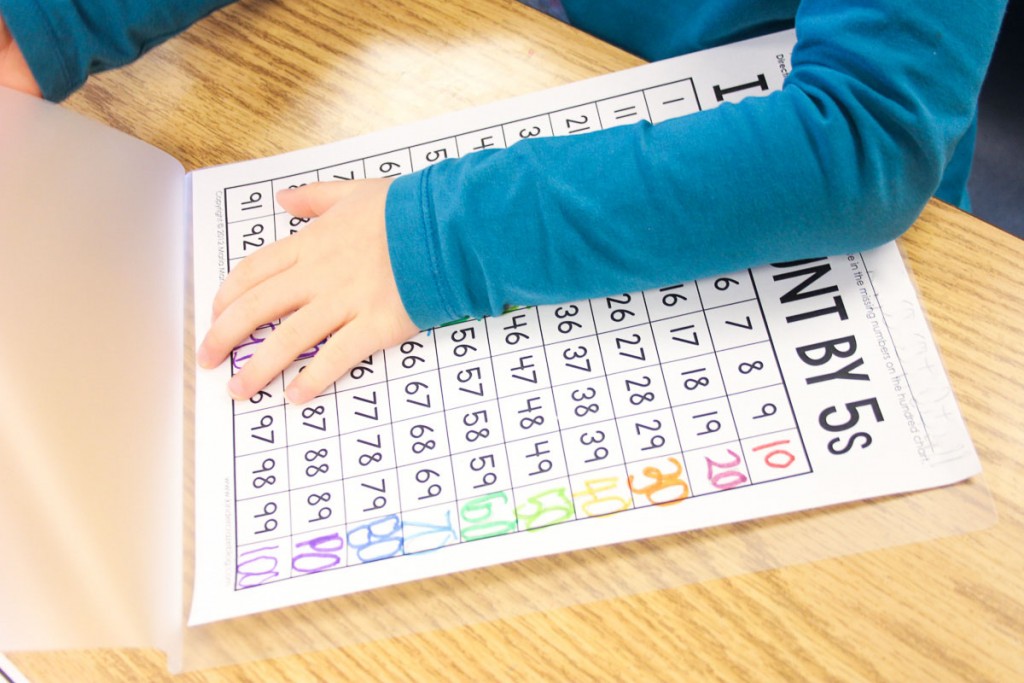 kindergarten student sitting at a table and placing skip counting practice page in a laminating sheet