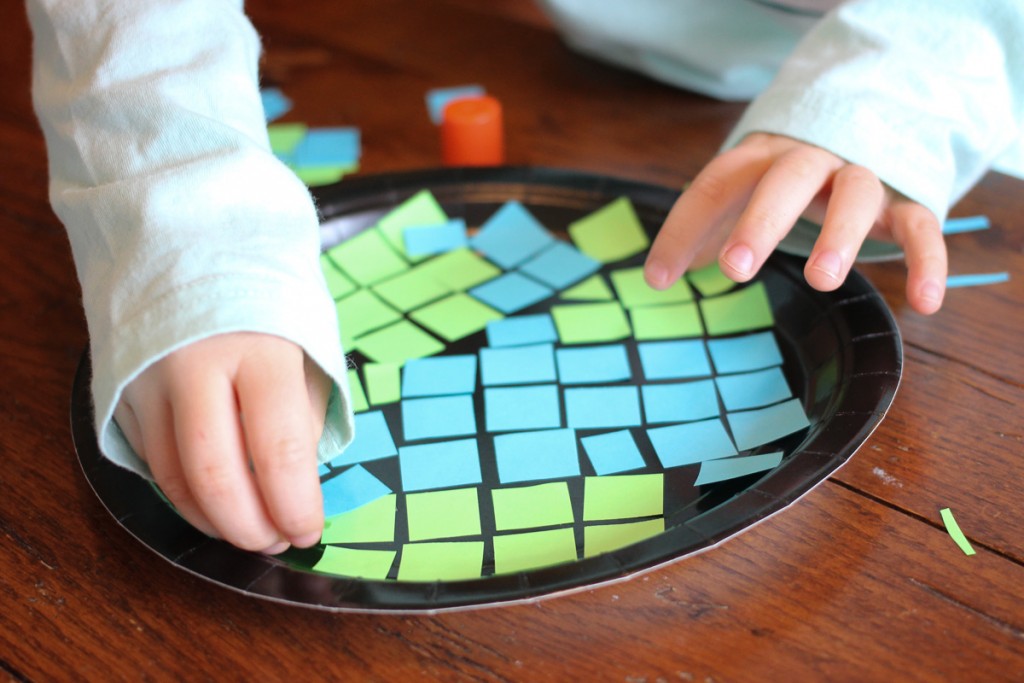young child glueing blue and green squares to create a simple earth day mosaic craft