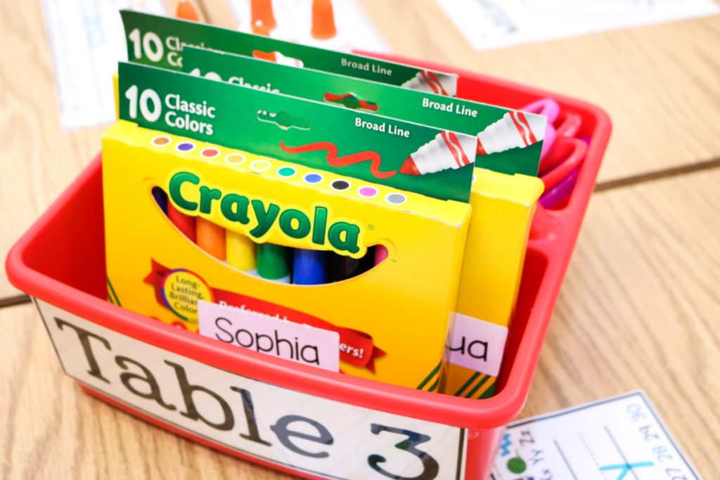 crayola markers labeled with student names in a red plastic table caddy on a classroom desk