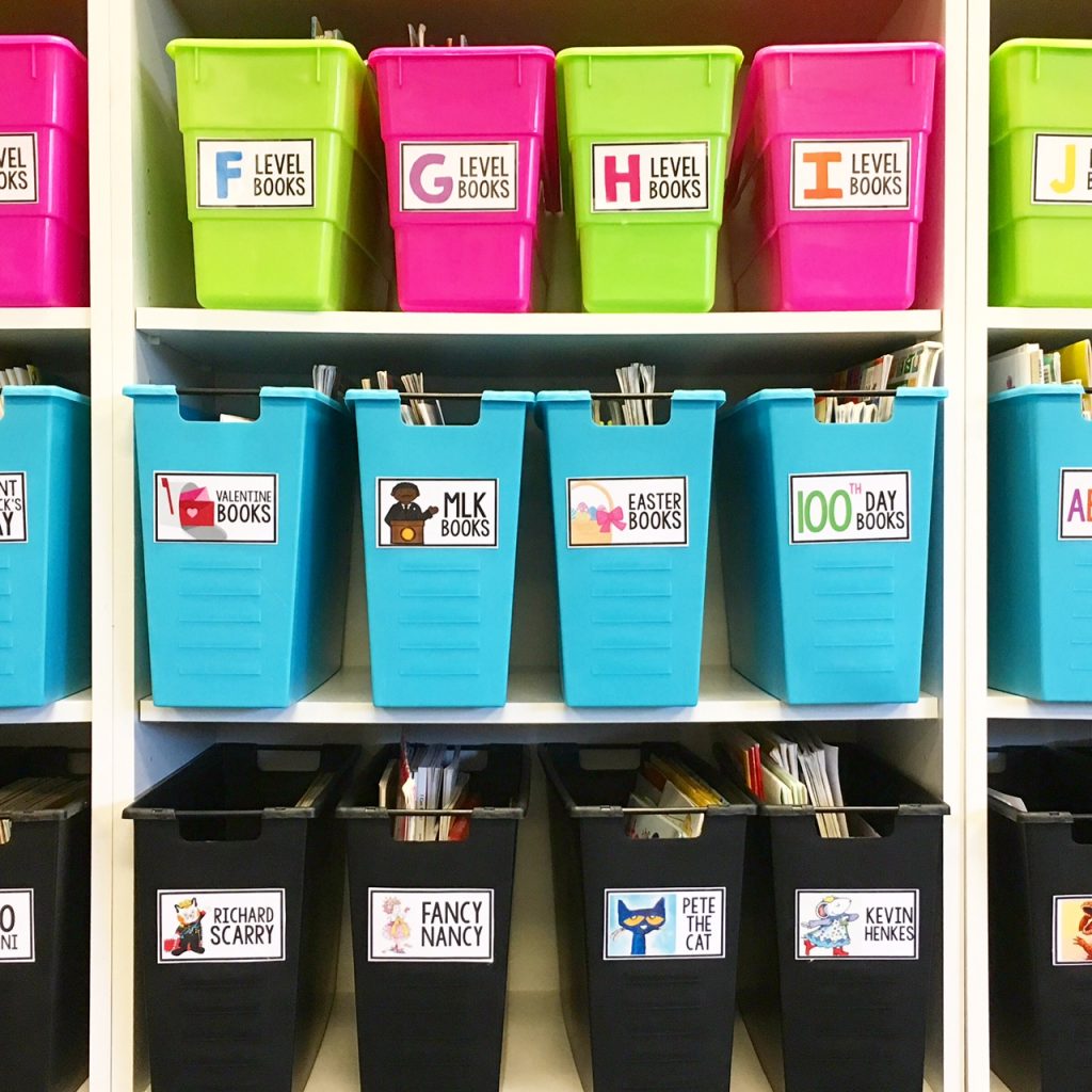 brightly colored bins in a first grade classroom library arranged on a white bookshelf and organized with classroom library labels