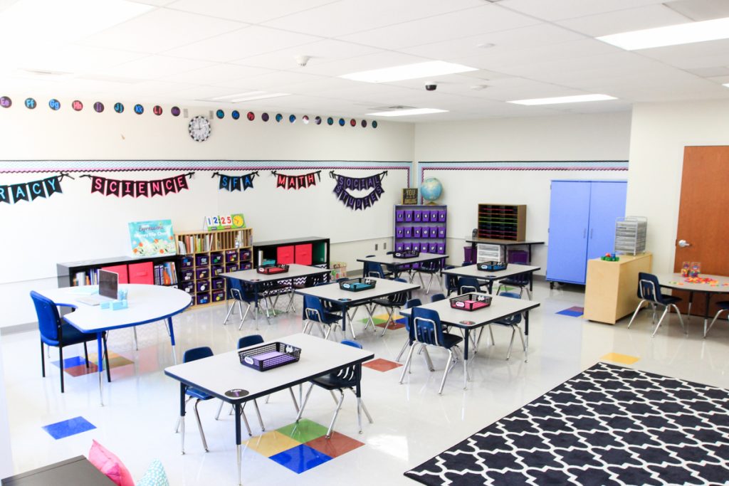 student tables in first grade classroom with subject areas displayed on the wall