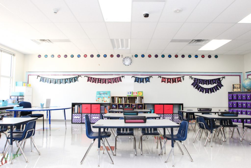 white and airy first grade classroom with pops of pink and purple bulletin board pennant letters displayed on whiteboard