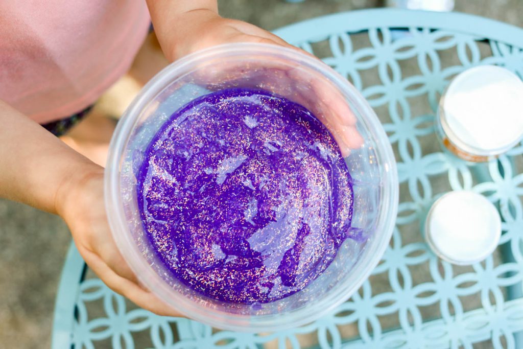 child holding a bowl of purple glitter glue to make slime at home
