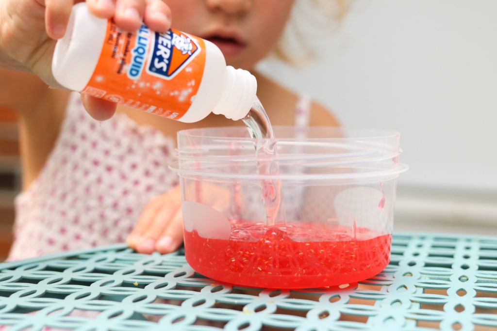 child pouring Elmers magical liquid into glitter glue to make slime at home