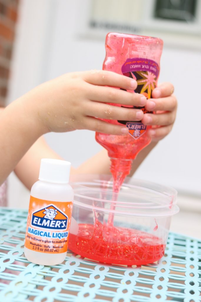 child squirting red glitter glue into a bowl to make slime