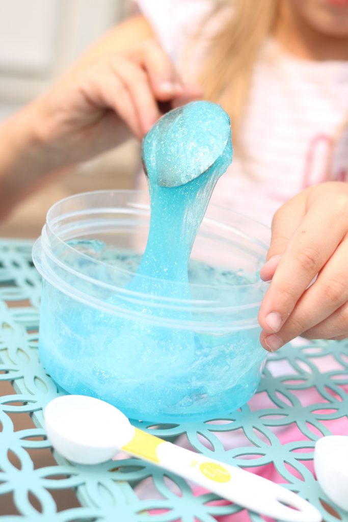 child mixing ingredients to make blue slime at home