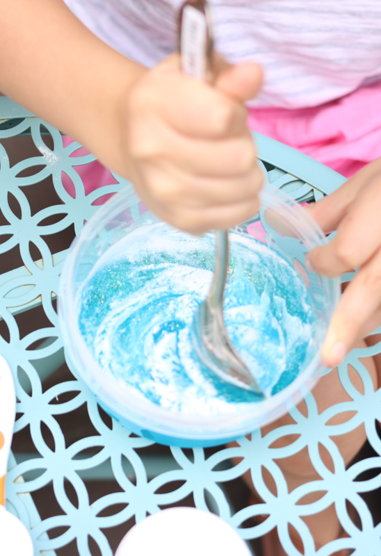 child stirring blue glitter glue with baking soda to make slime at home