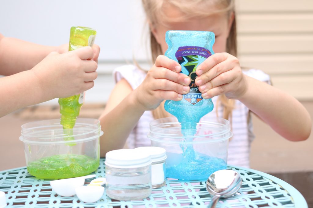 children squirting glue into bowls to create their own slime at home