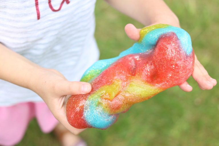 child holding red, blue and yellow slime to make your own rainbow slime at home