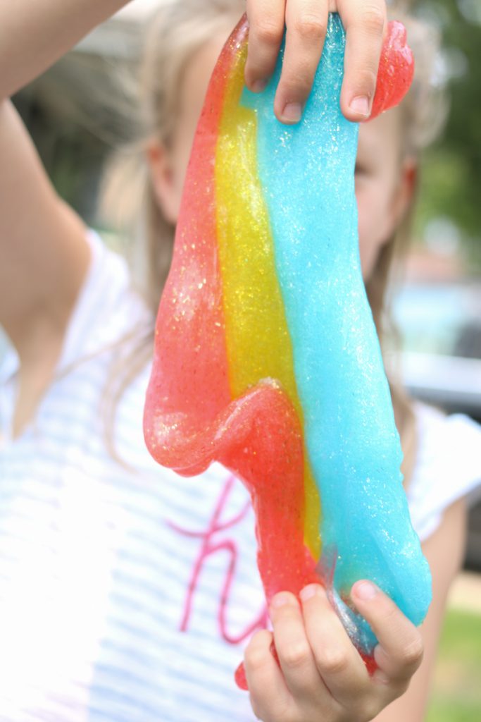 child holding blue, yellow and red rainbow slime