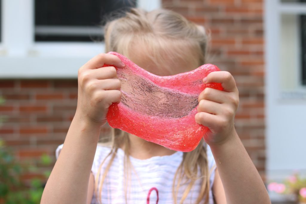 child holding up stretched out red glitter slime