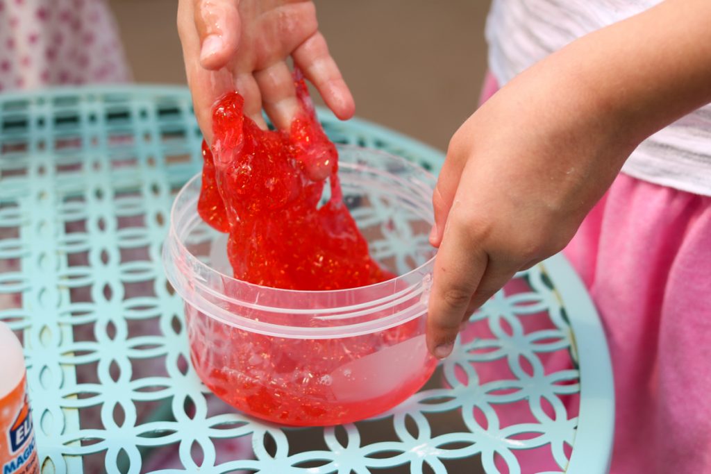 child making red rainbow glitter slime at home