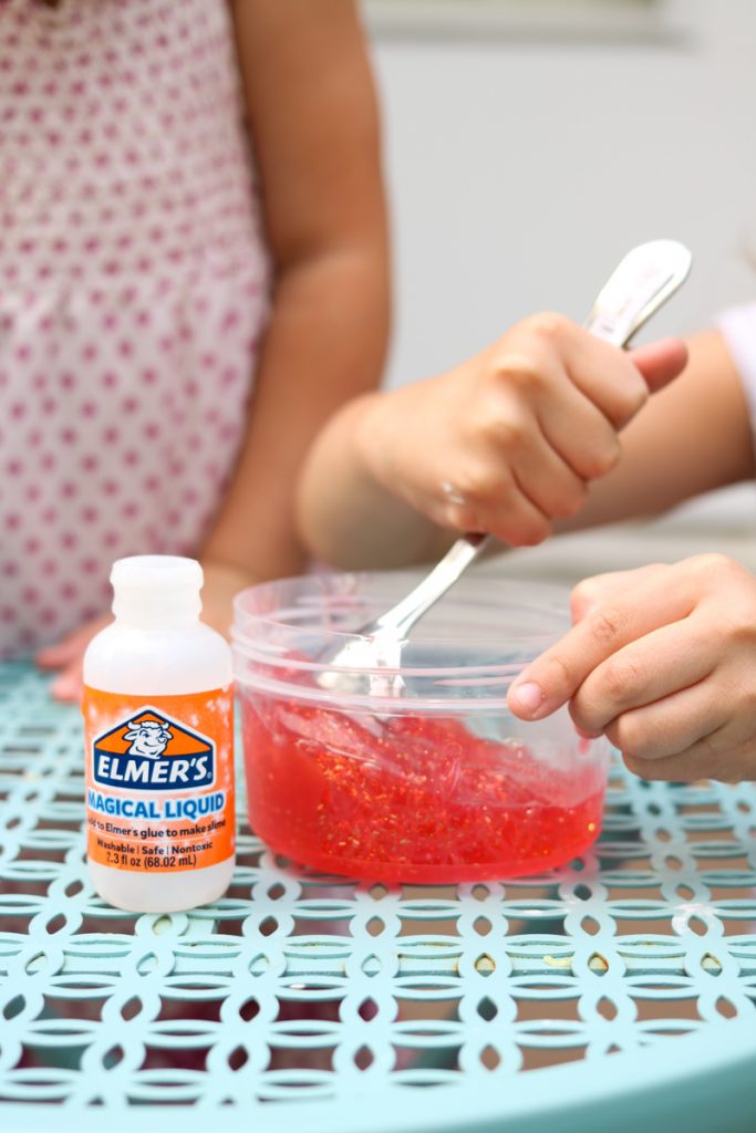 child stirring magical liquid into elmers red glitter glue to make easy slime at home