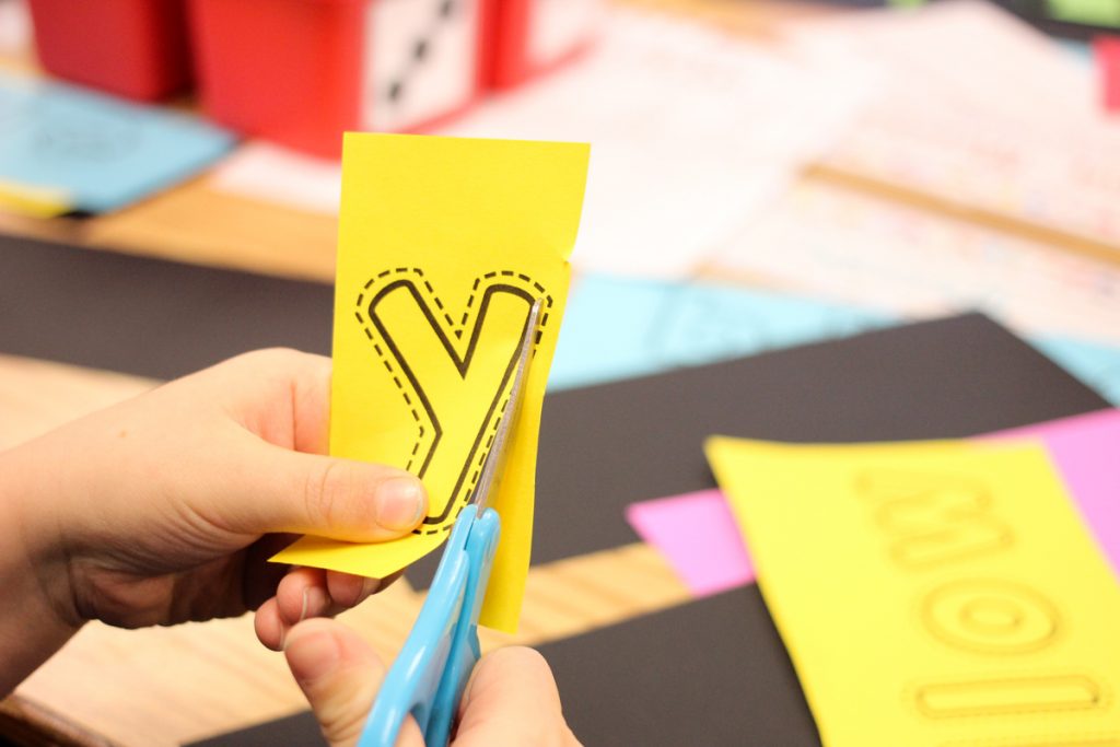 child cutting out the letter y from a piece of yellow paper to work on color word worksheets