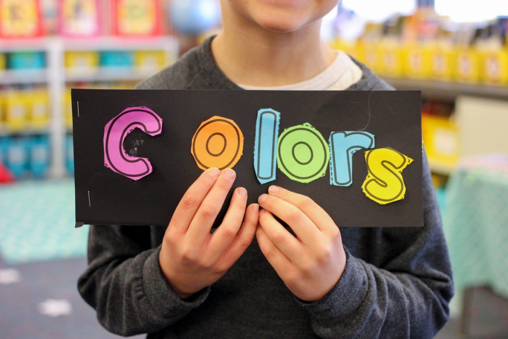 child in classroom holding up "colors" book instead of color word worksheets