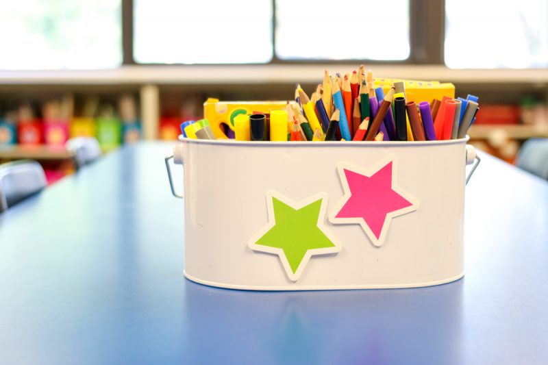 classroom supply bin with markers and crayons and star cutouts on the front
