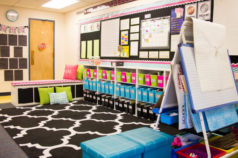 first grade classroom library with black carpet and brightly colored book bins that are labeled with book contents